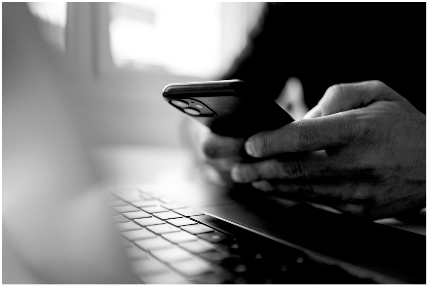 Hands holding a phone in front of a laptop