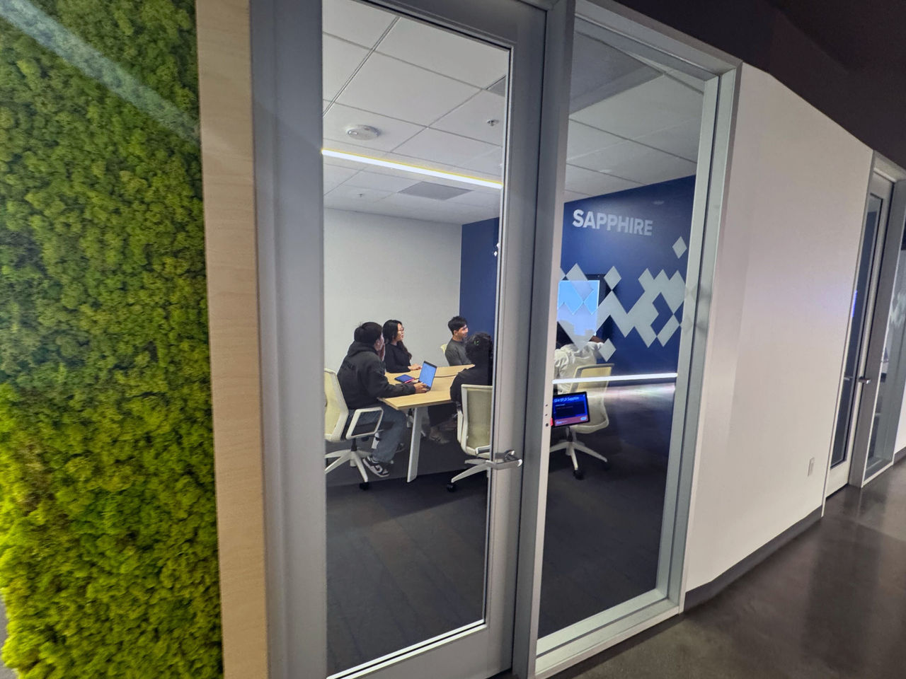 A glass-walled meeting room featuring a Sapphire-branded wall and modern furnishings. 