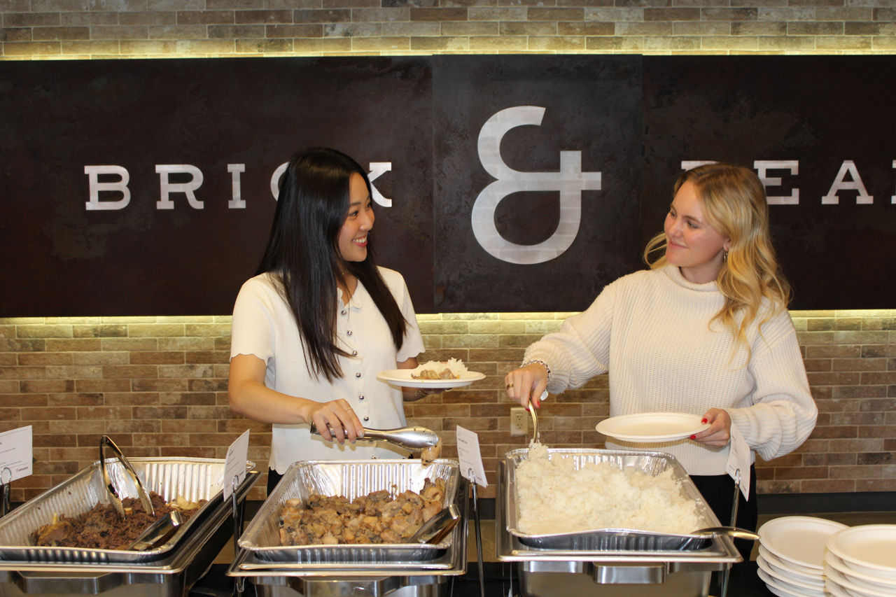 Two individuals are serving food from a buffet setup at a restaurant.